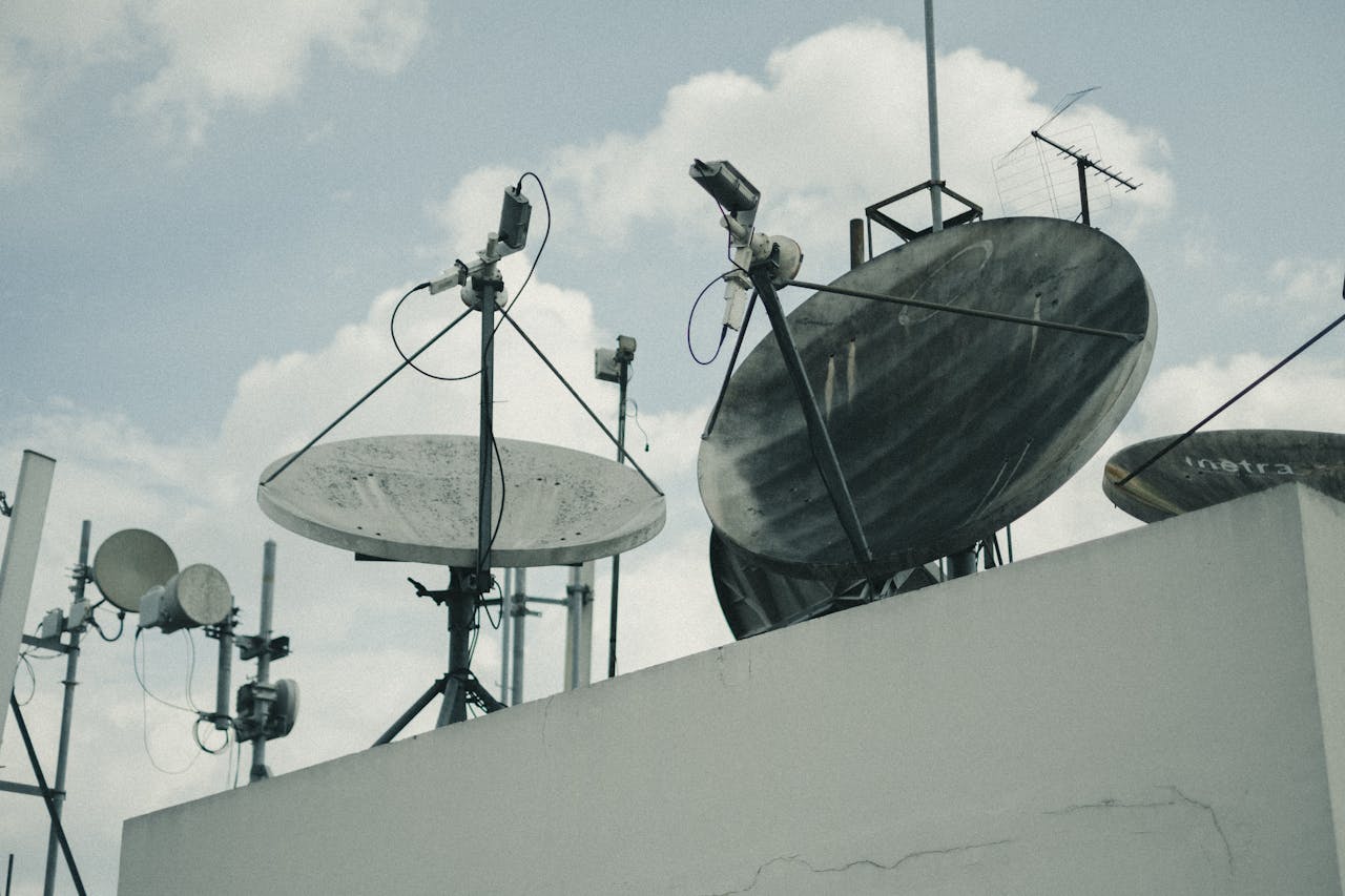 A detailed view of satellite dishes and antennas on an urban rooftop under a cloudy sky.